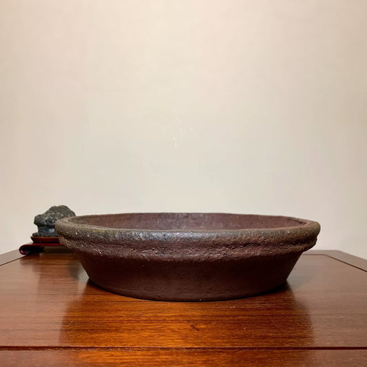 Dark brown, shallow, unglazed ceramic pot with rough texture and slightly raised rim.