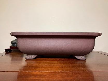 A matte purple rectangular pot with four curved feet, unglazed surface.