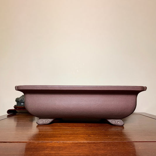 A matte purple rectangular pot with four curved feet, unglazed surface.