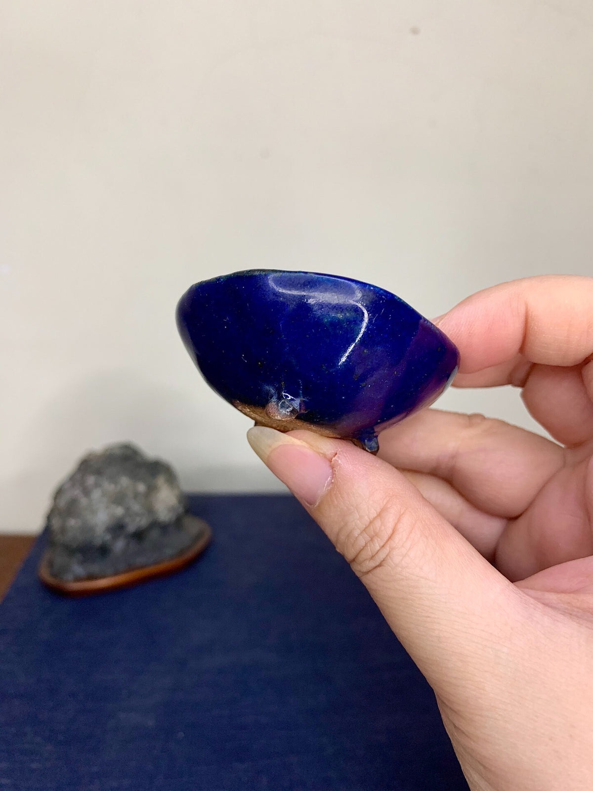 A hand holds a glossy, deep blue, rounded pot with a brown rim and a small white mark.