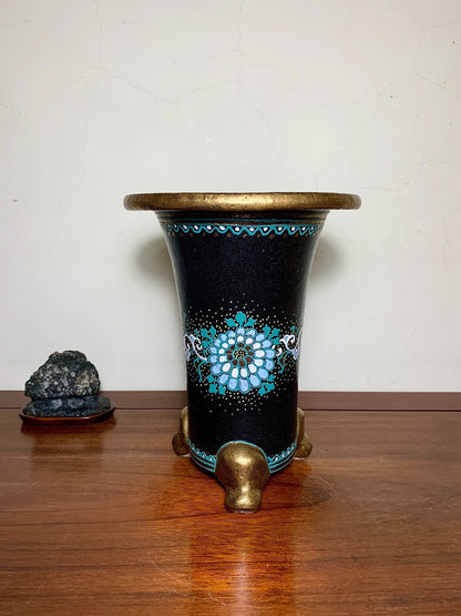 Black glazed pot with gold rim and three feet, featuring a blue floral pattern.