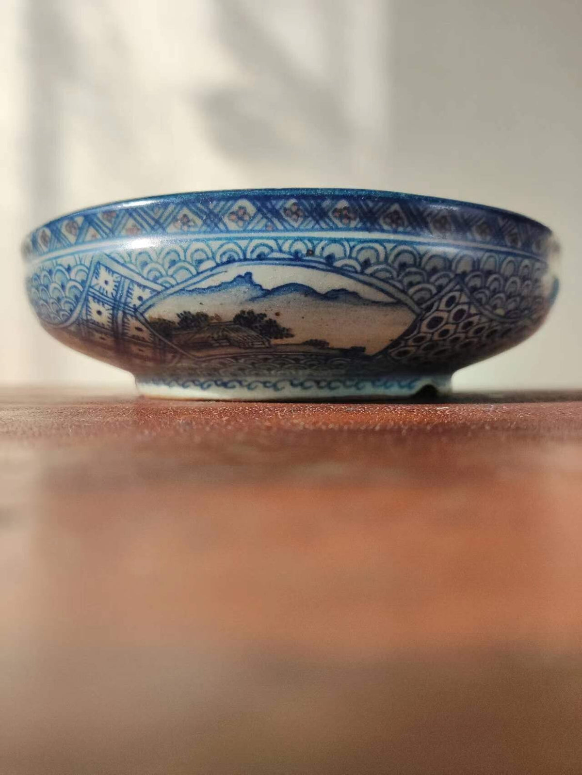 A blue and white glazed ceramic bowl with a landscape scene and decorative border.
