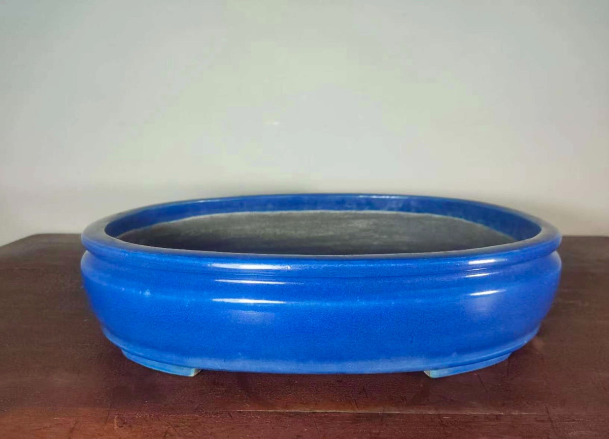 A glossy, vibrant blue ceramic pot with a wide rim and three feet, unadorned.
