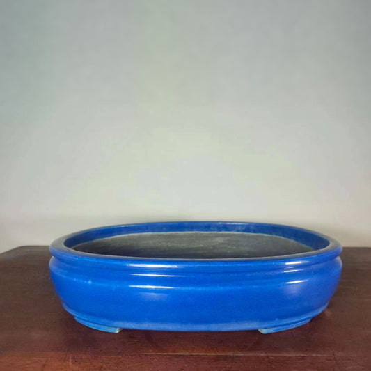A glossy, vibrant blue ceramic pot with a wide rim and three feet, unadorned.