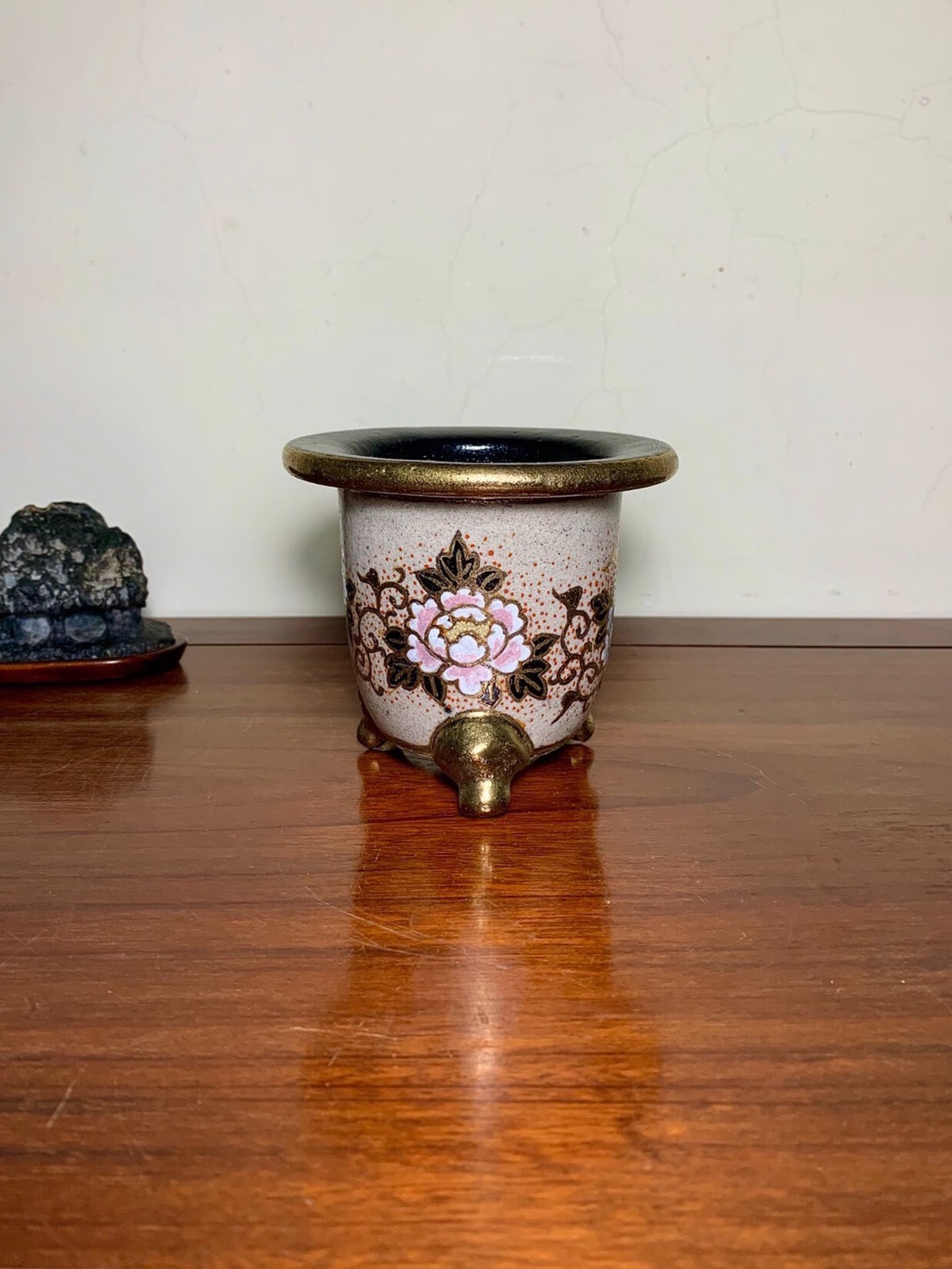 A small, light-colored ceramic pot with a black rim and a pink floral design on its side.