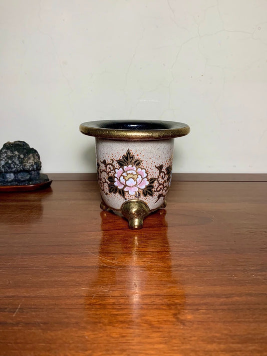 A small, light-colored ceramic pot with a black rim and a pink floral design on its side.