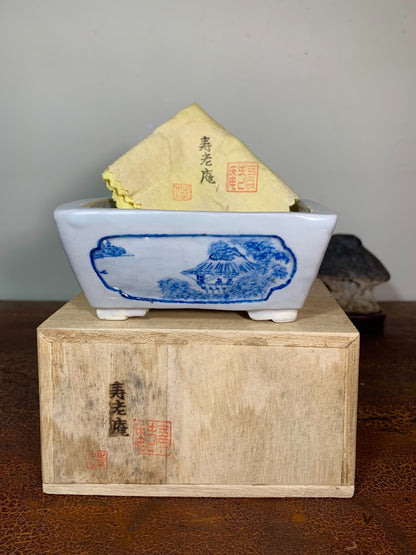 White rectangular ceramic pot with blue landscape painting, holding a yellow paper packet.