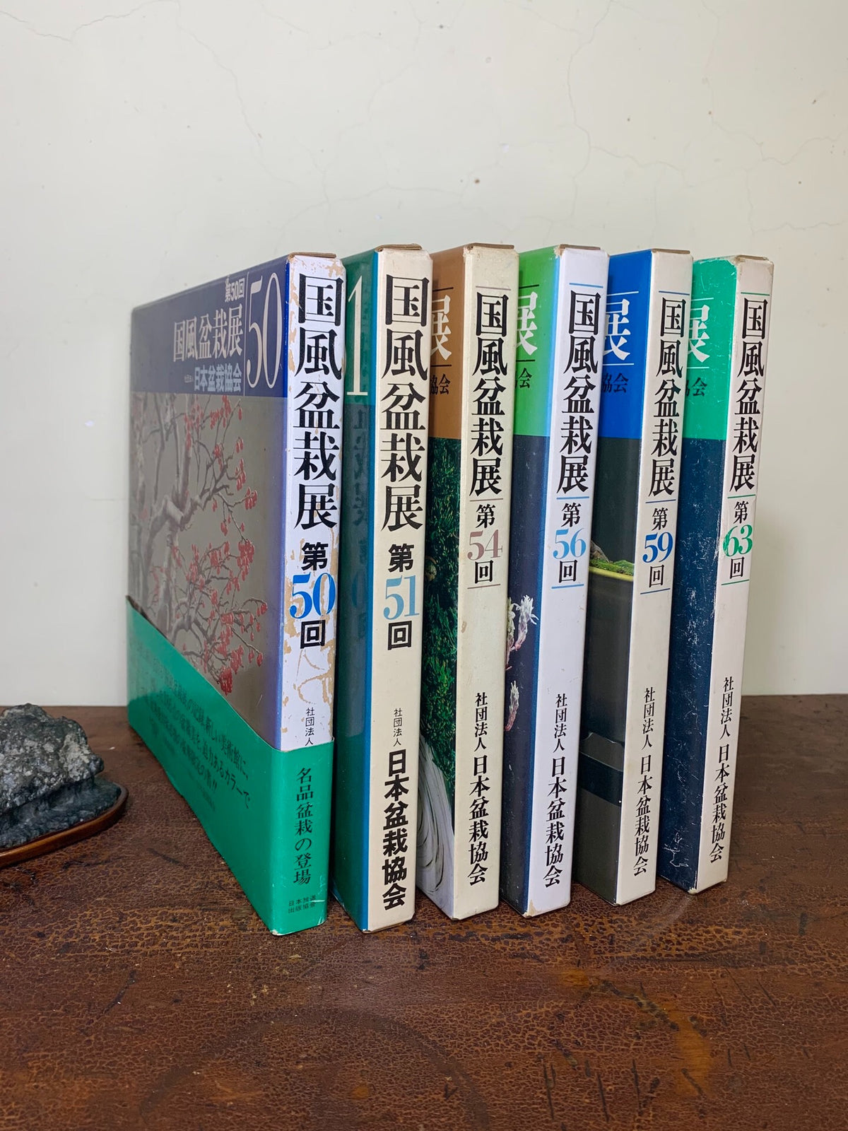 Six books with Japanese text and floral covers stand upright on a wooden surface.
