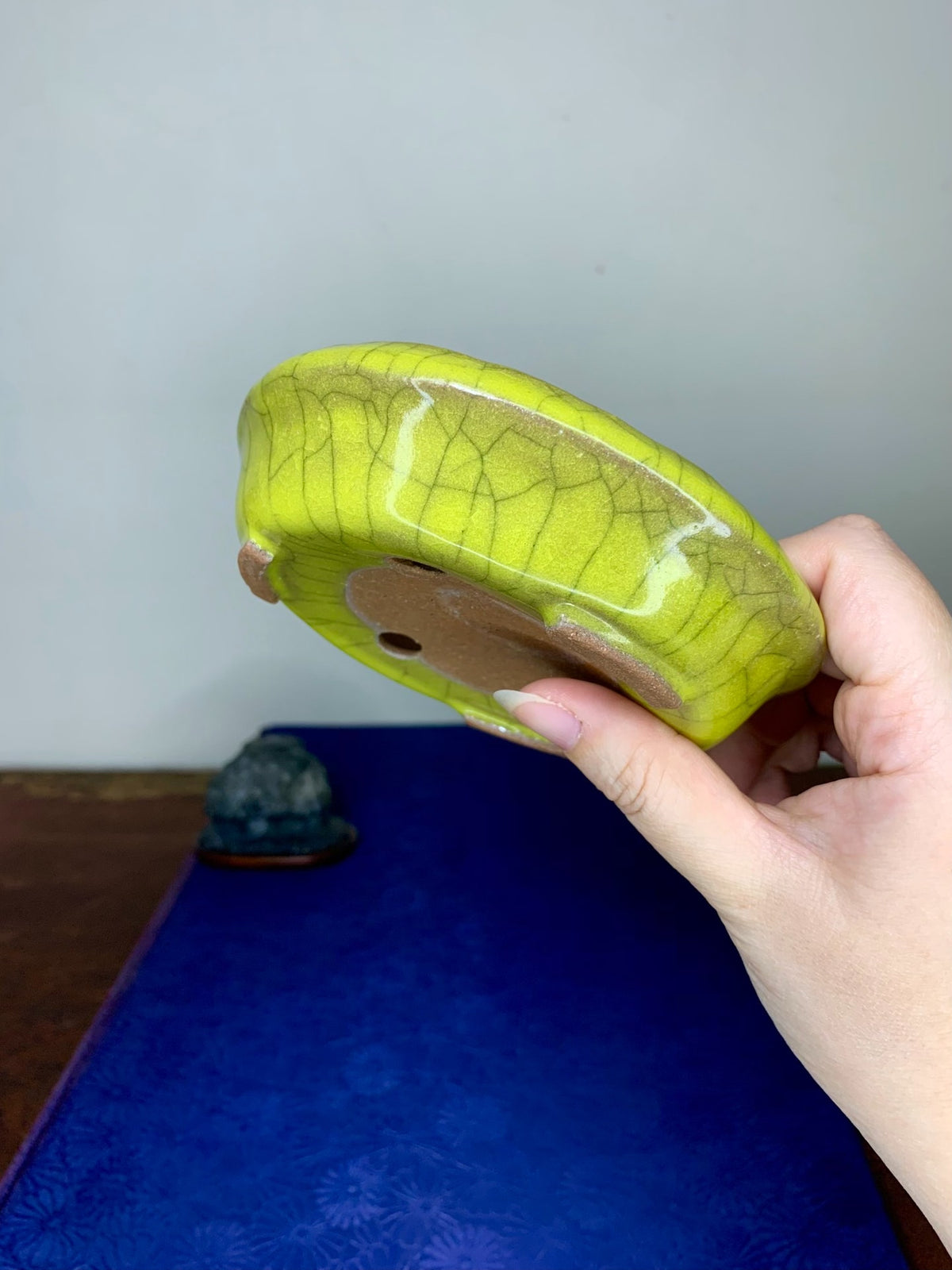 A hand holds a lime-green glazed pot with a crackled surface and a brown drainage hole.