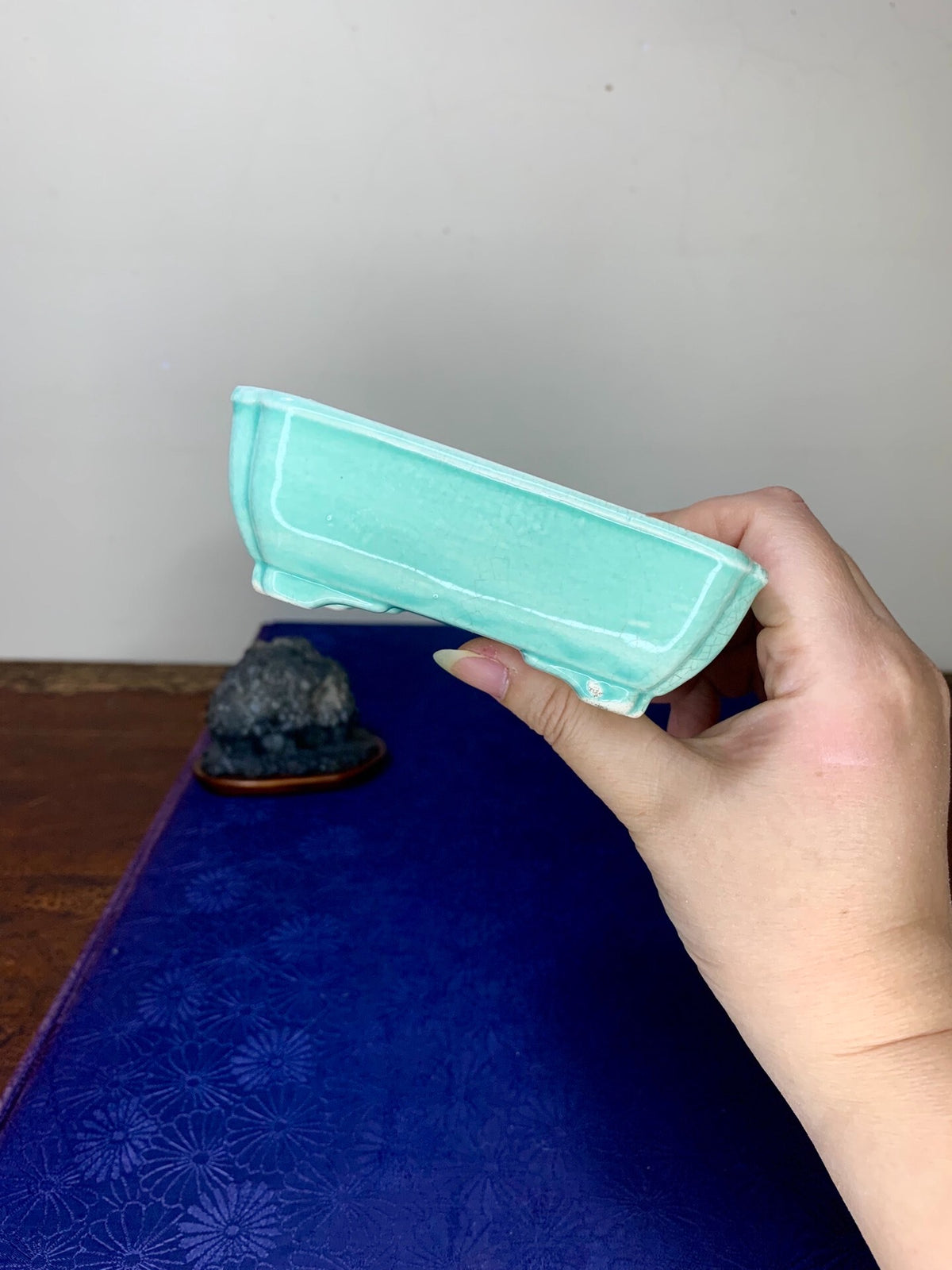 A hand holds a light turquoise glazed rectangular pot with a slightly raised rim.