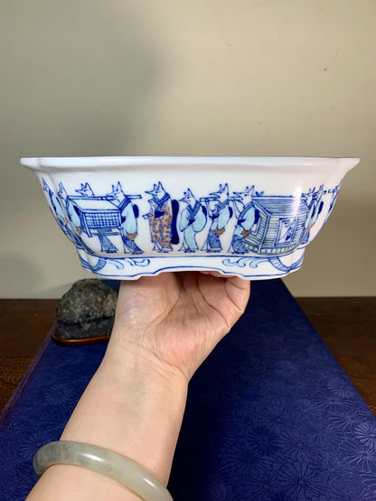 A hand holds a white glazed ceramic bowl with blue painted figures and patterns.