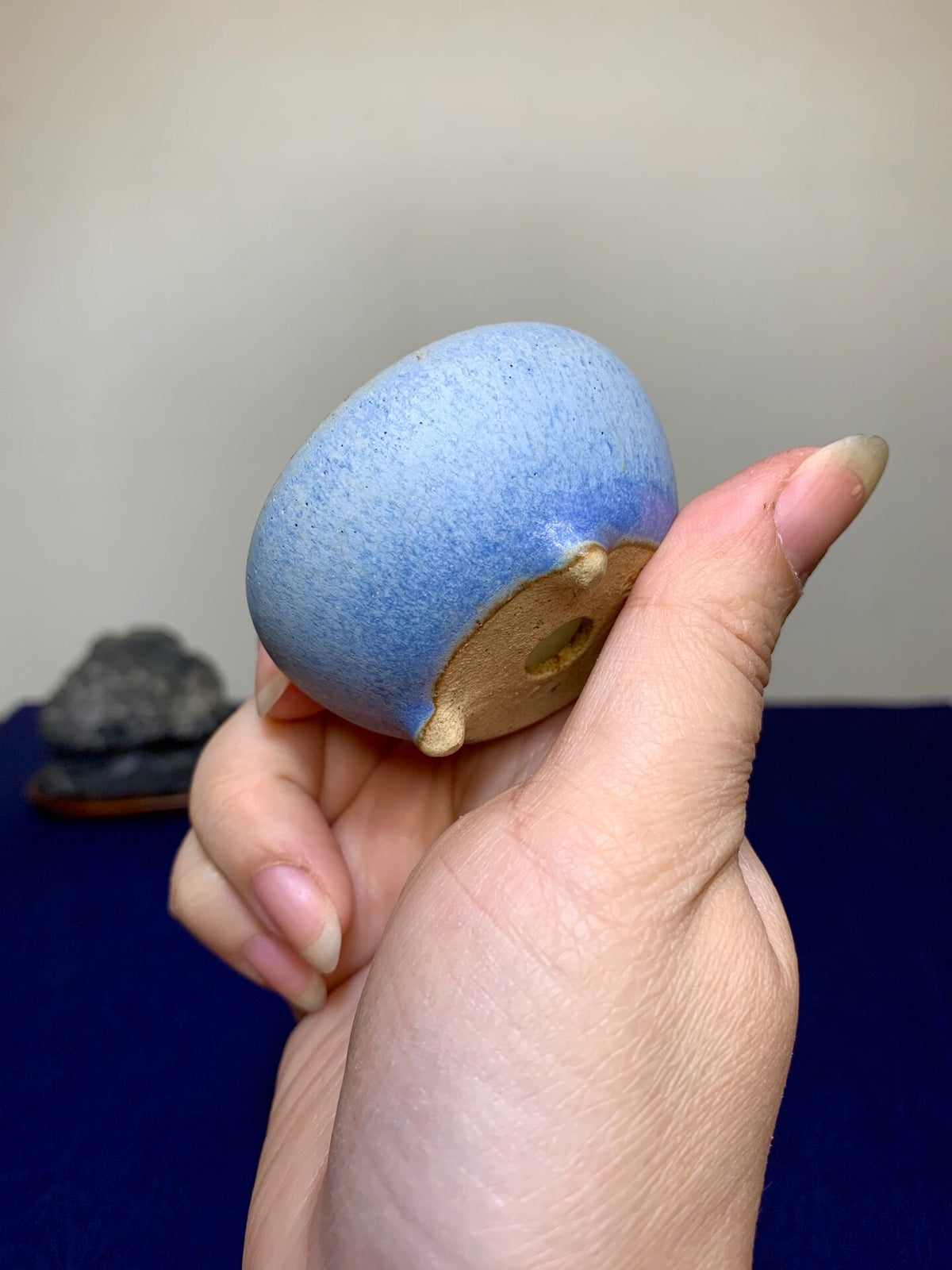 A hand holds a small, blue-glazed ceramic pot with a brown unglazed base and drainage hole.
