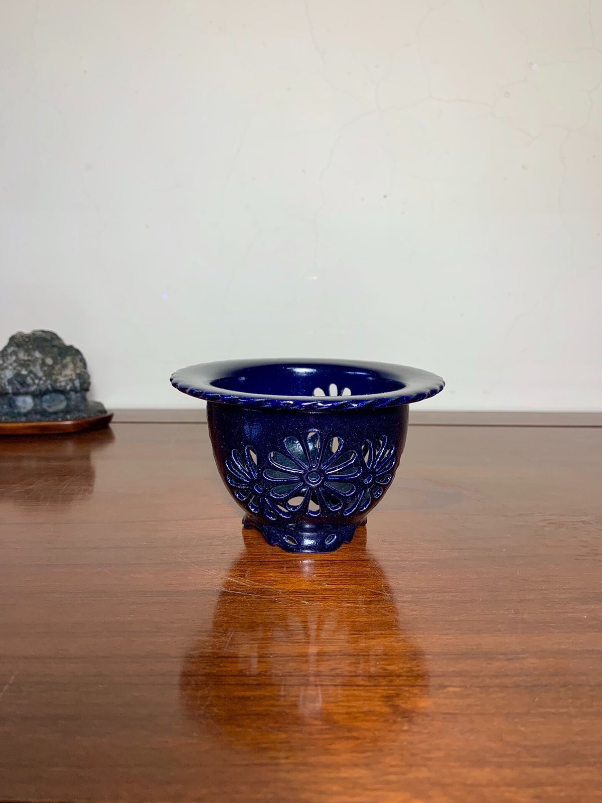 A deep blue glazed ceramic pot with a raised floral pattern and scalloped rim.
