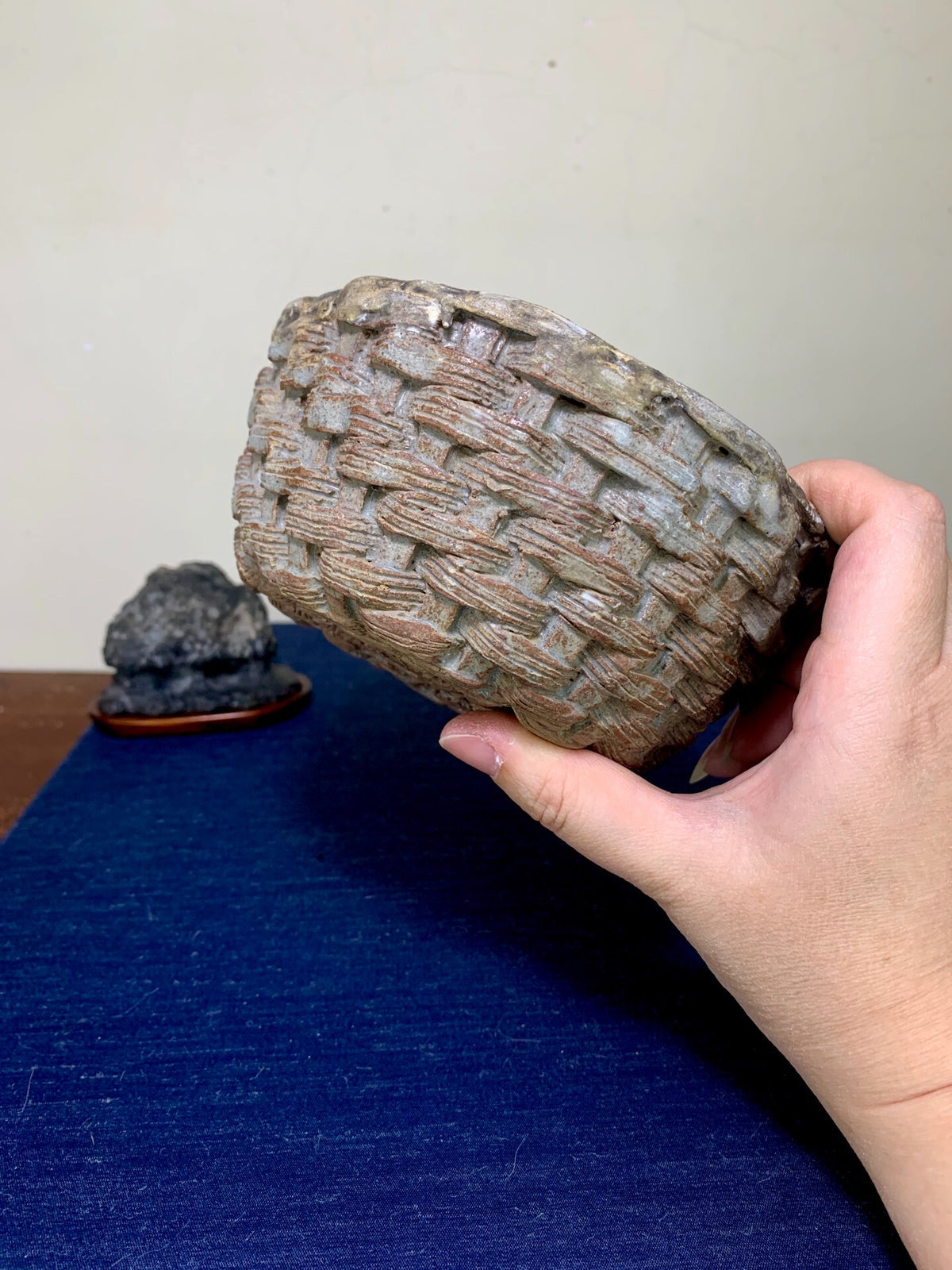 A hand holds a small, grey, woven-textured pot with a matte finish.
