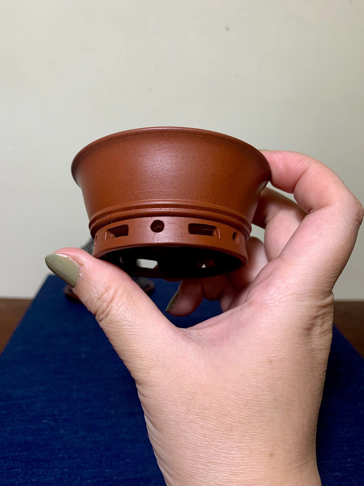 A hand holds a small, unglazed terracotta pot with a flared rim and drainage holes.