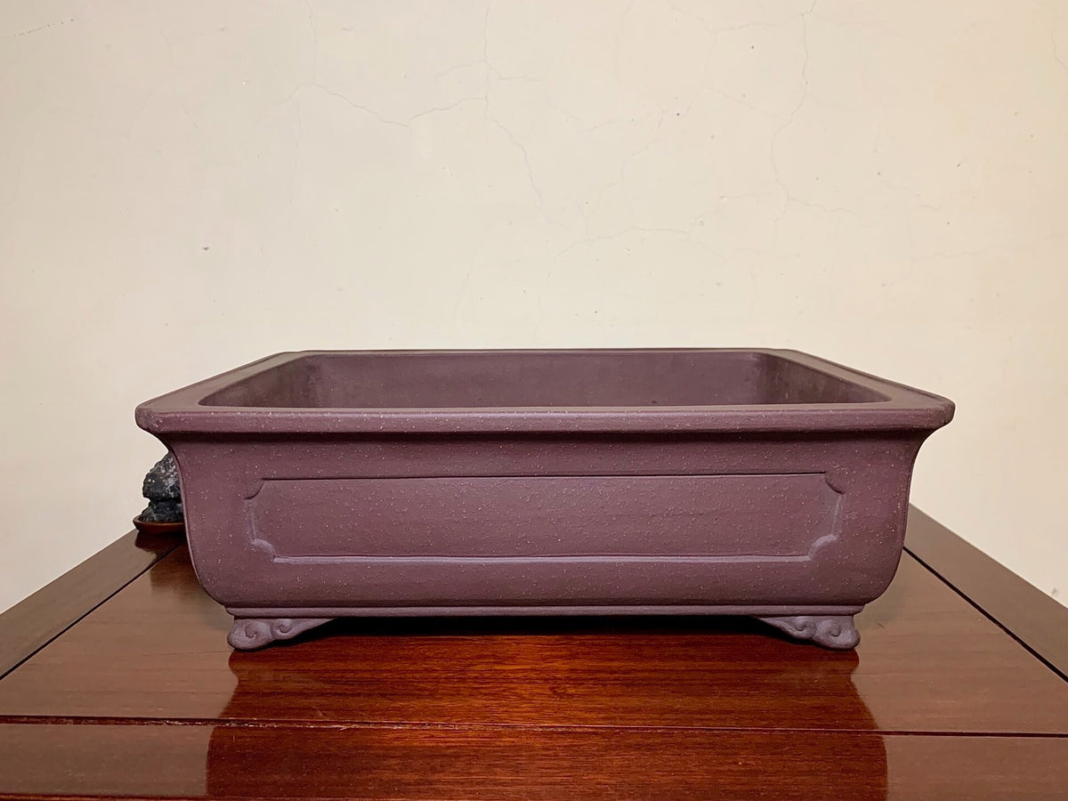 A matte purple rectangular pot with raised panel and four feet, unglazed surface.