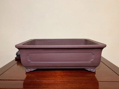 A matte purple rectangular pot with raised panel and four feet, unglazed surface.