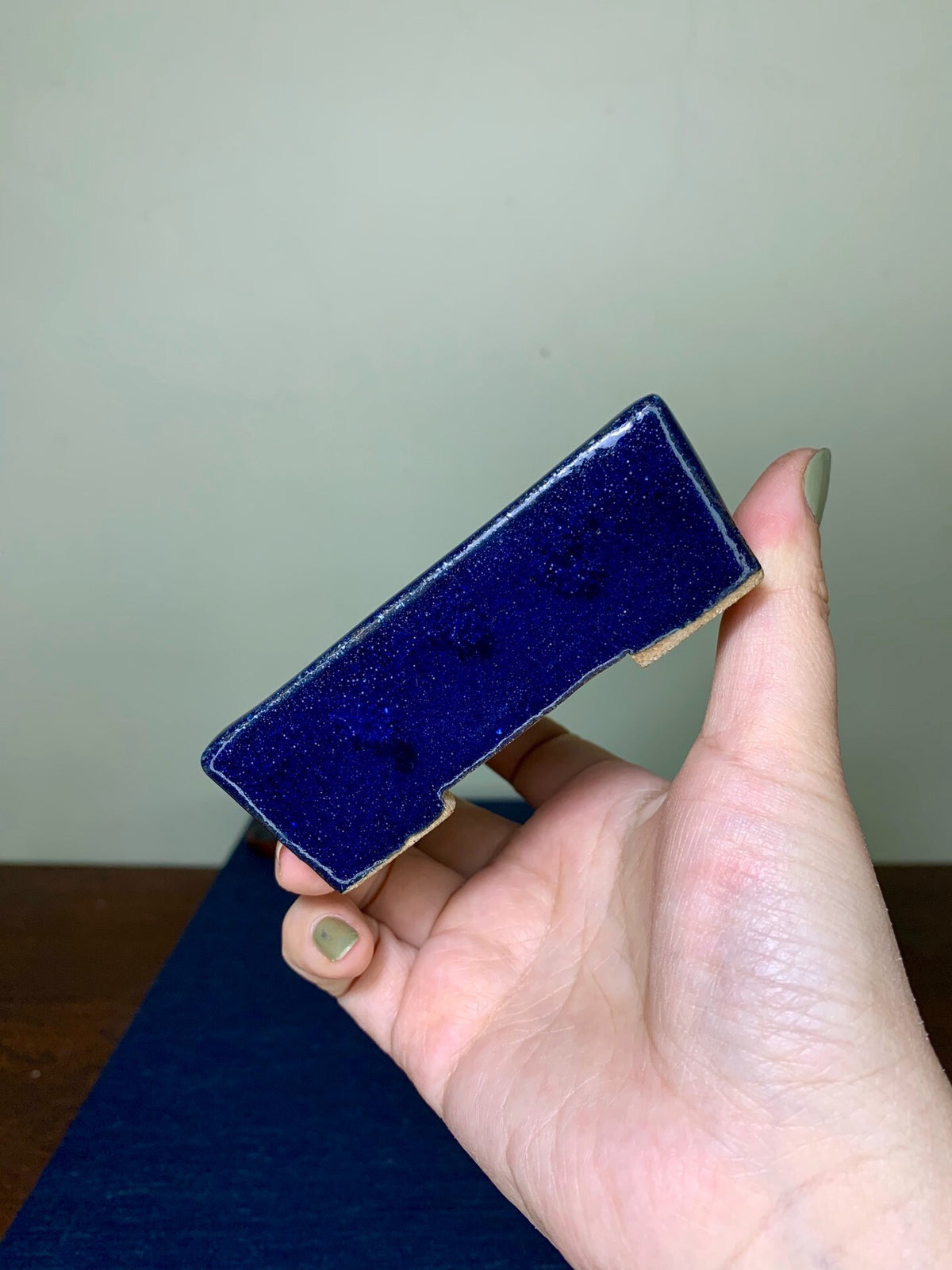 A hand holds a small, rectangular, glossy cobalt blue glazed pot with a light brown rim.