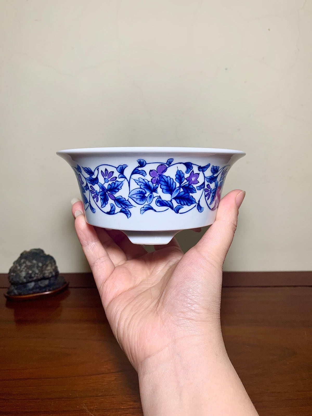 A hand holds a white ceramic bowl with a blue floral pattern around its rim.