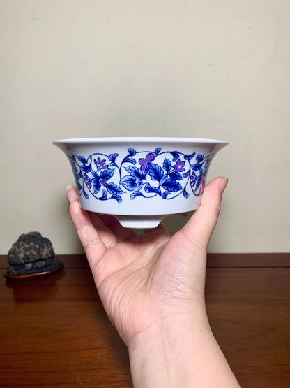 A hand holds a white ceramic bowl with a blue floral pattern around its rim.
