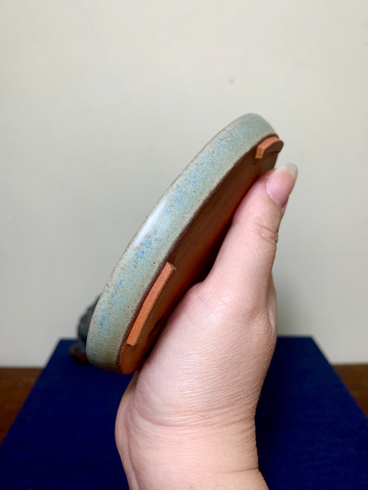 Hand holds a shallow, glazed grey-blue ceramic pot with exposed terracotta rim and foot.