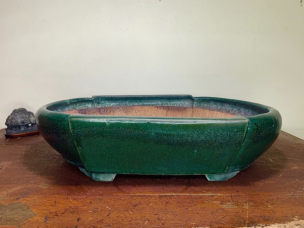 Dark green glazed rectangular pot with rounded edges and four feet, sitting on a wooden surface.