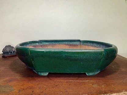 Dark green glazed rectangular pot with rounded edges and four feet, sitting on a wooden surface.