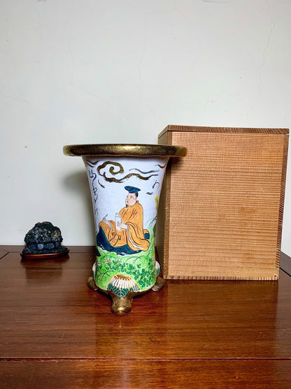 White glazed pot with painted figure, gold rim and feet, beside wooden box.