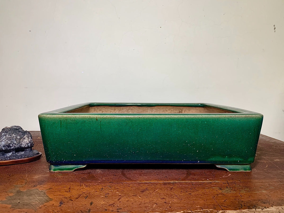 A glossy, deep green rectangular pot with a matte brown interior sits on a wooden surface.