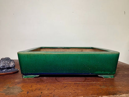 A glossy, deep green rectangular pot with a matte brown interior sits on a wooden surface.