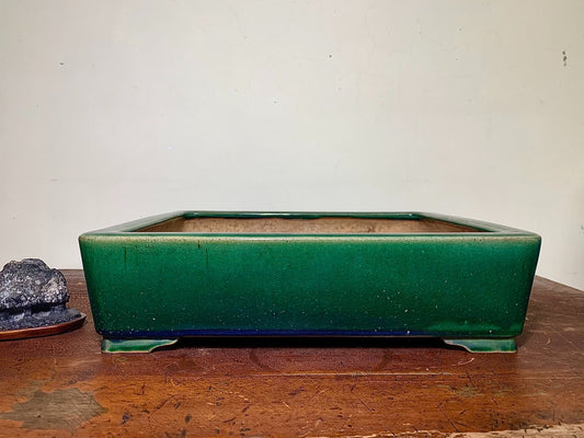 A glossy, deep green rectangular pot with a matte brown interior sits on a wooden surface.