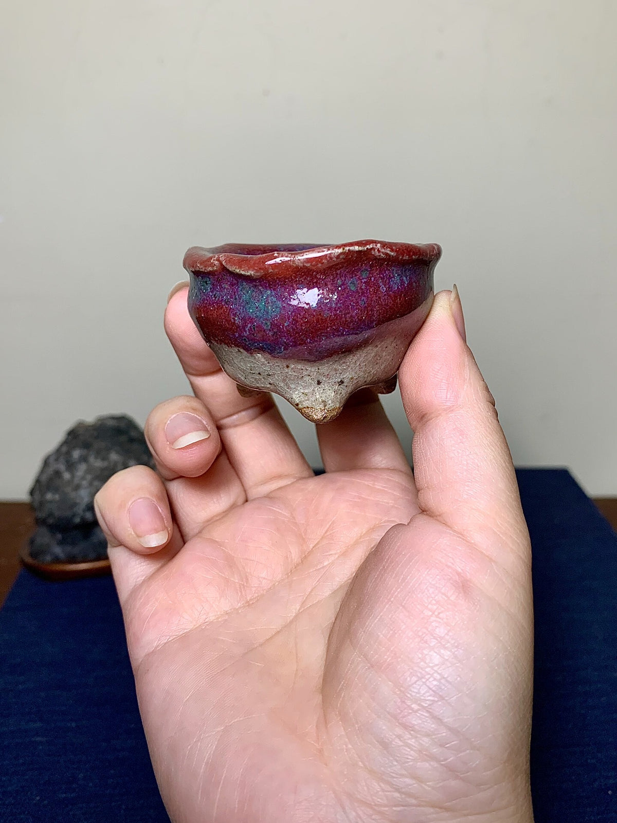 A hand holds a small, glazed ceramic pot with a vibrant purple and blue glaze rim.