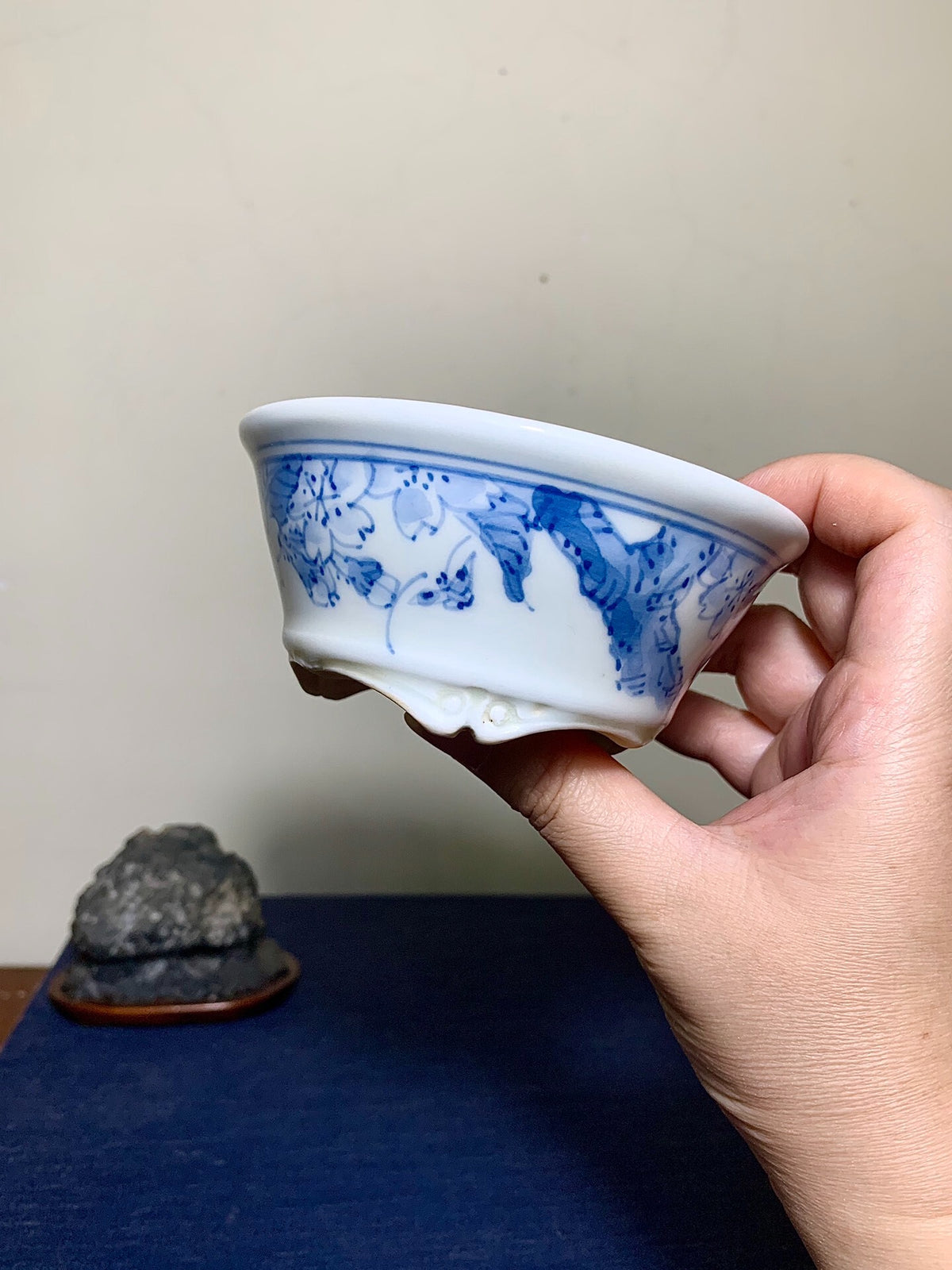 A hand holds a white glazed ceramic pot with blue floral and leaf patterns.