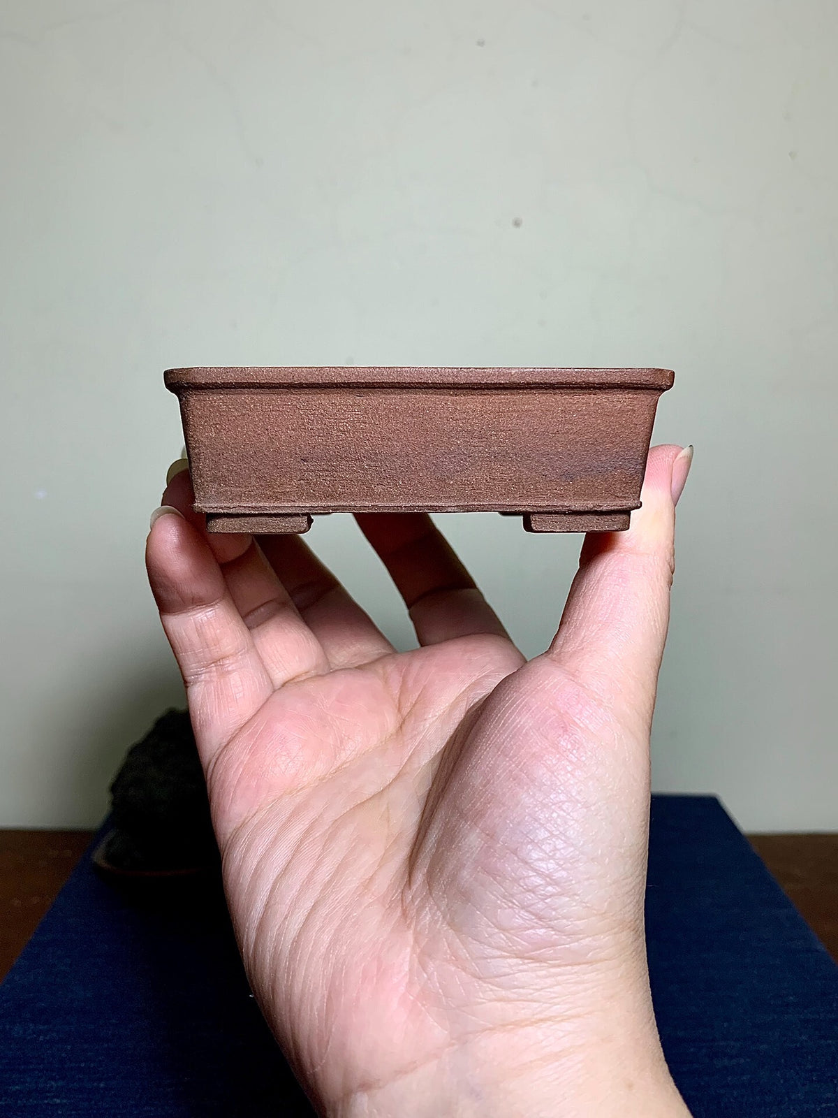 A small, rectangular, unglazed brown ceramic pot held in a hand.