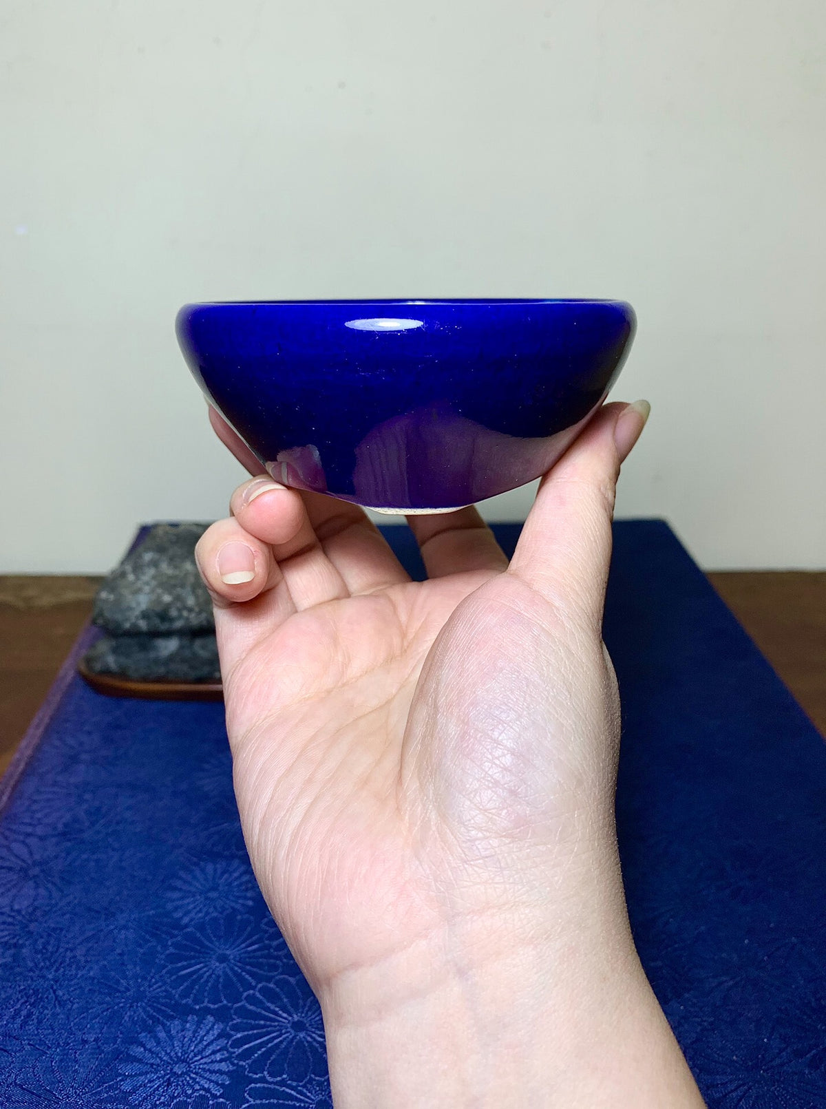 A hand holds a small, glossy cobalt blue ceramic bowl with a smooth, rounded rim.