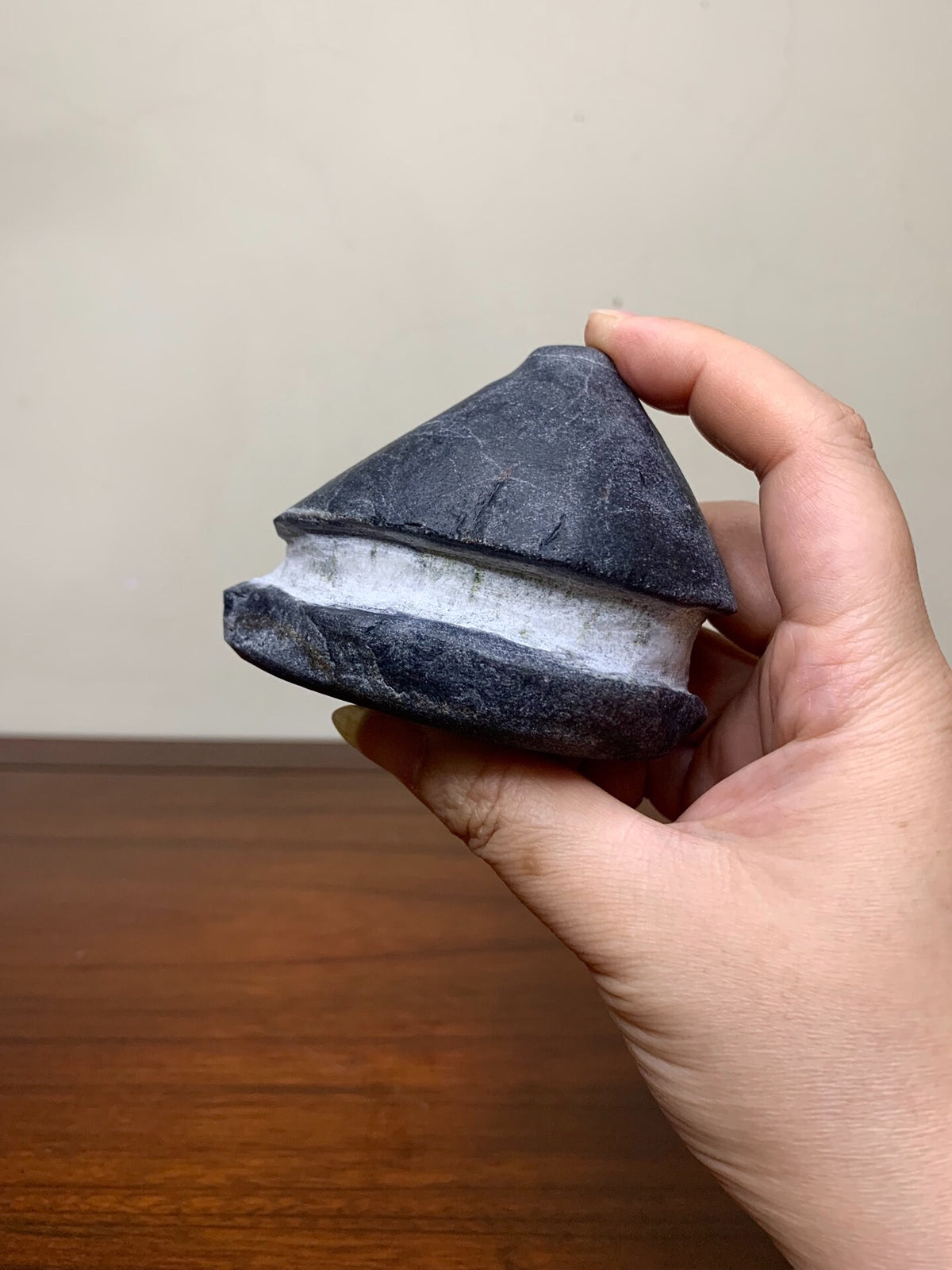 A hand holds a dark grey, conical stone pot with a white glazed band around its base.