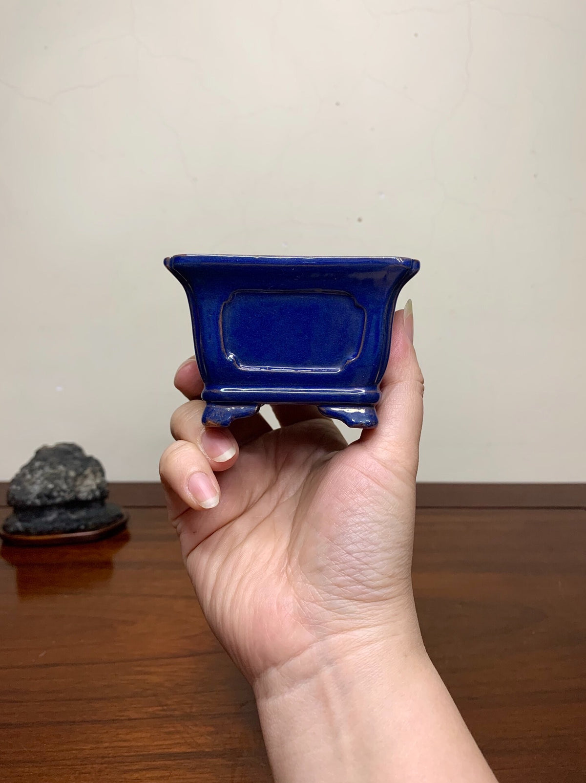A hand holds a small, deep blue glazed rectangular pot with a recessed center panel.