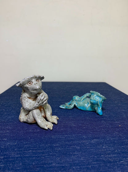 Two small figurines: one grey speckled monkey in a hat, one turquoise reclining animal.