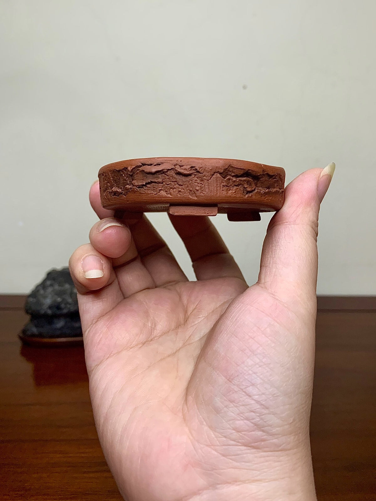 A small, unglazed reddish-brown ceramic pot base with textured, cracked surface held in hand.