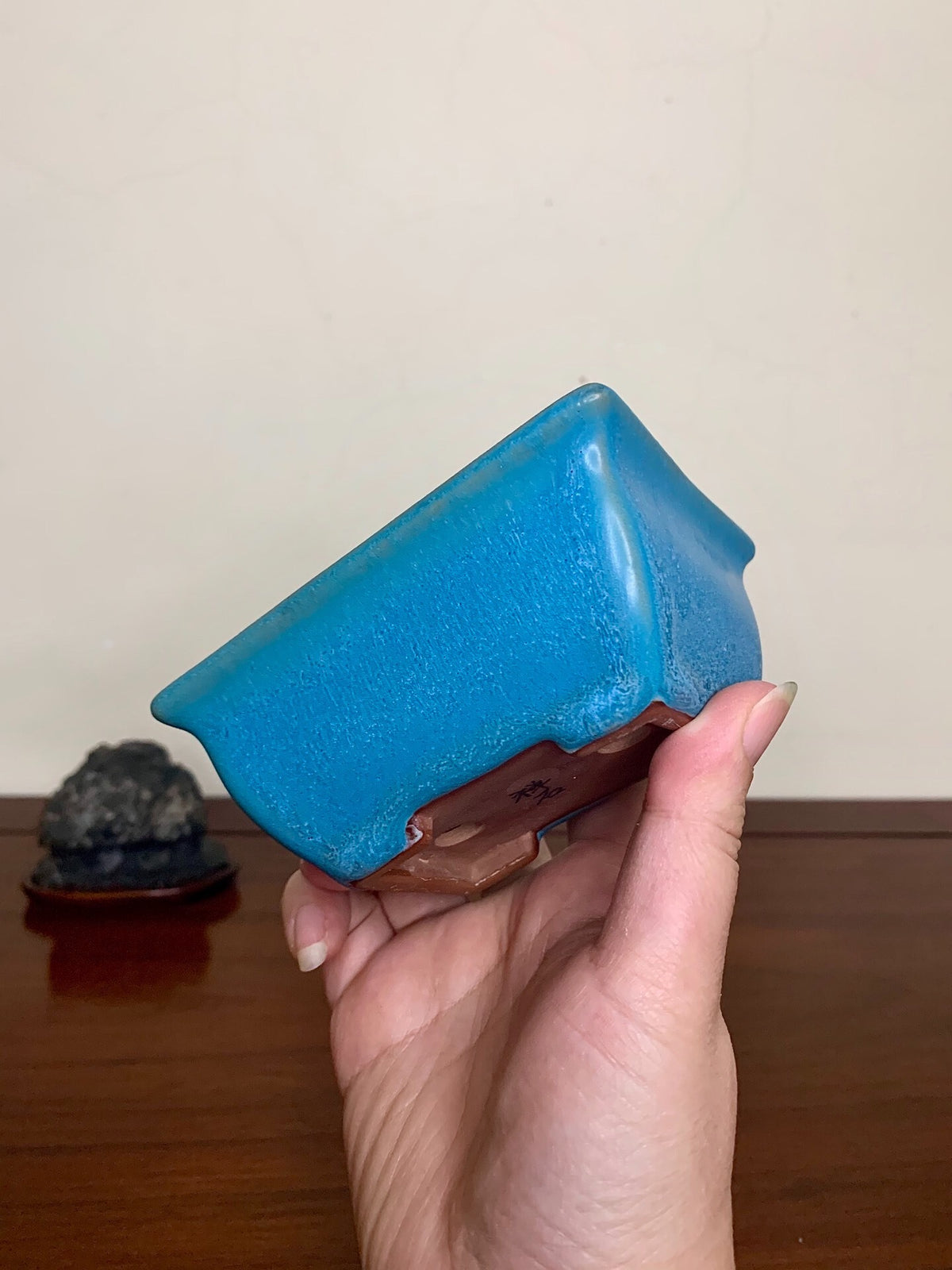 A hand holds a glossy, bright blue rectangular pot with a brown unglazed base.