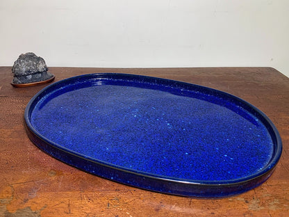 A glossy cobalt blue oval tray with glittery speckles sits on a wooden surface.