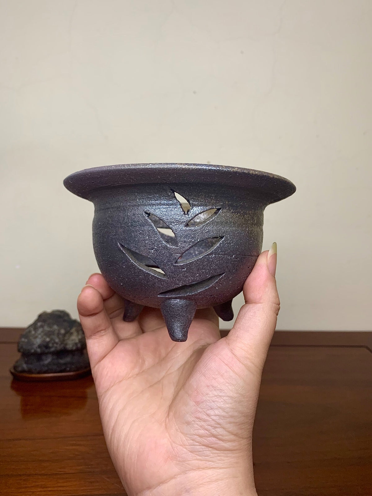 Dark brown glazed pot with leaf-shaped cutouts, held in hand.