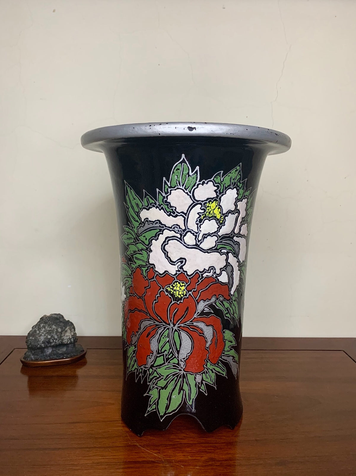 Black glazed pot with red and white floral design, flared rim, sits on wooden surface.