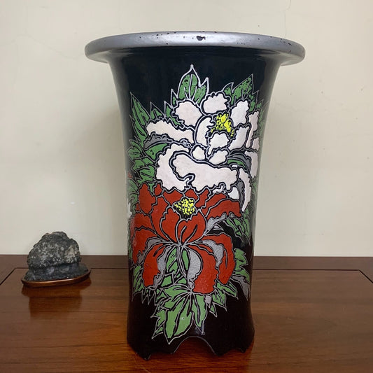 Black glazed pot with red and white floral design, flared rim, sits on wooden surface.