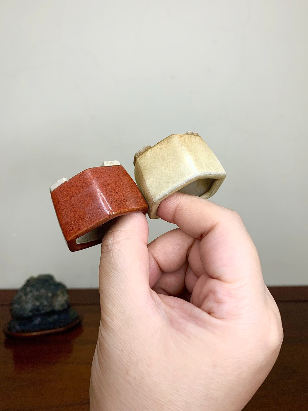 Two small, glazed ceramic pots, one reddish-brown, one beige, held in hand.