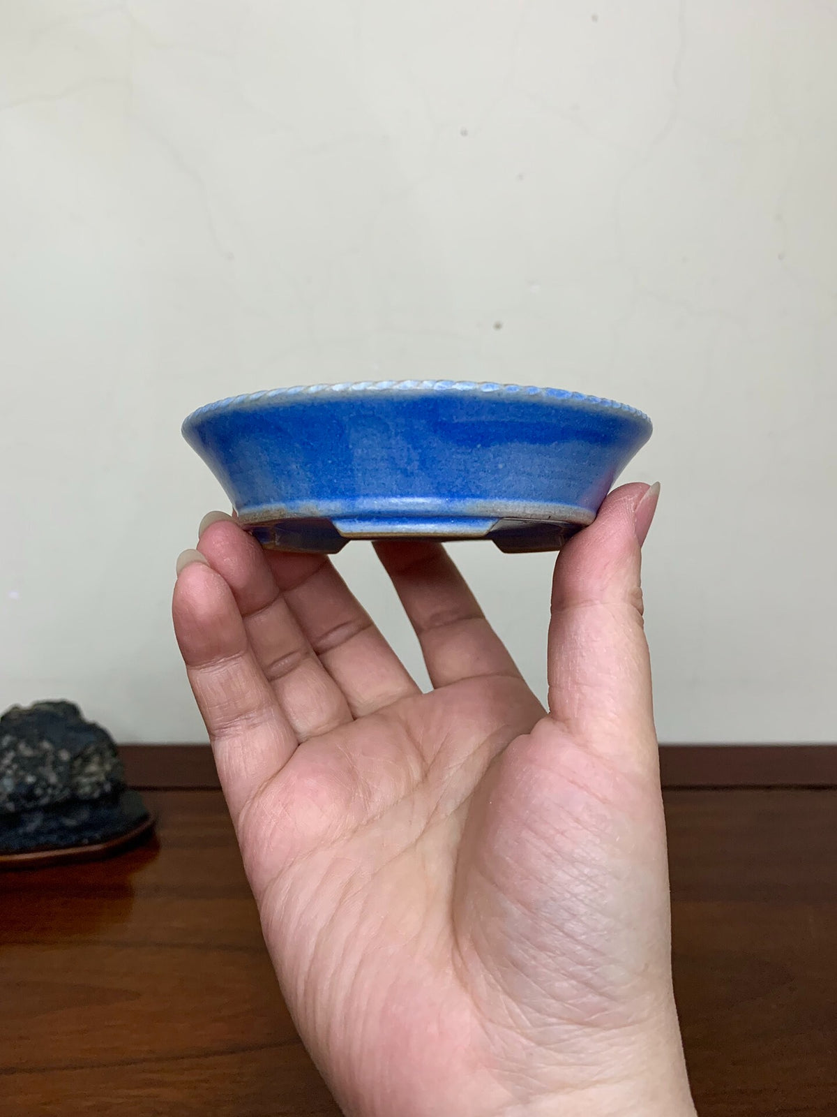 A hand holds a small, glossy blue glazed pot with a flared rim and unglazed base.