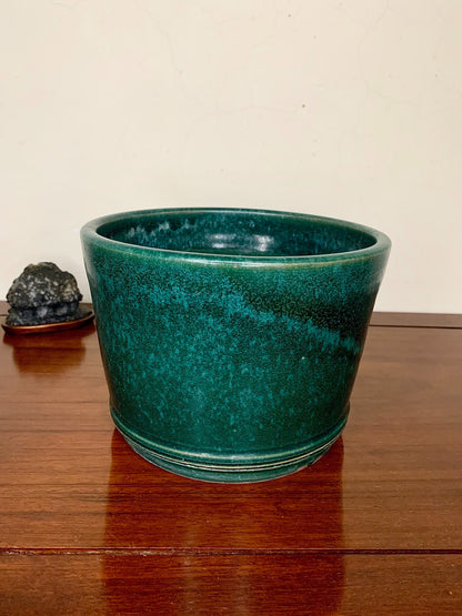 A glossy teal ceramic pot with a flared rim and horizontal ridges near the base.