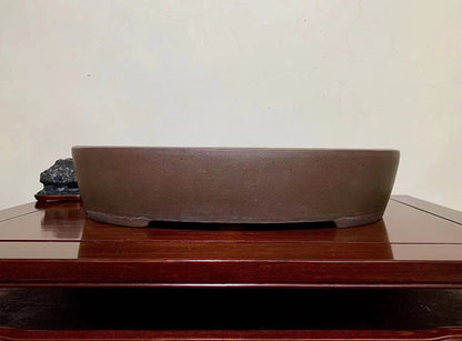 A matte brown unglazed ceramic pot with a wide, shallow, oval shape and a flat rim.