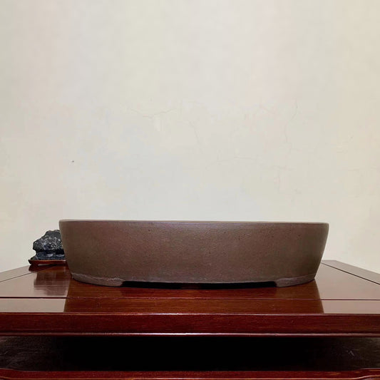 A matte brown unglazed ceramic pot with a wide, shallow, oval shape and a flat rim.