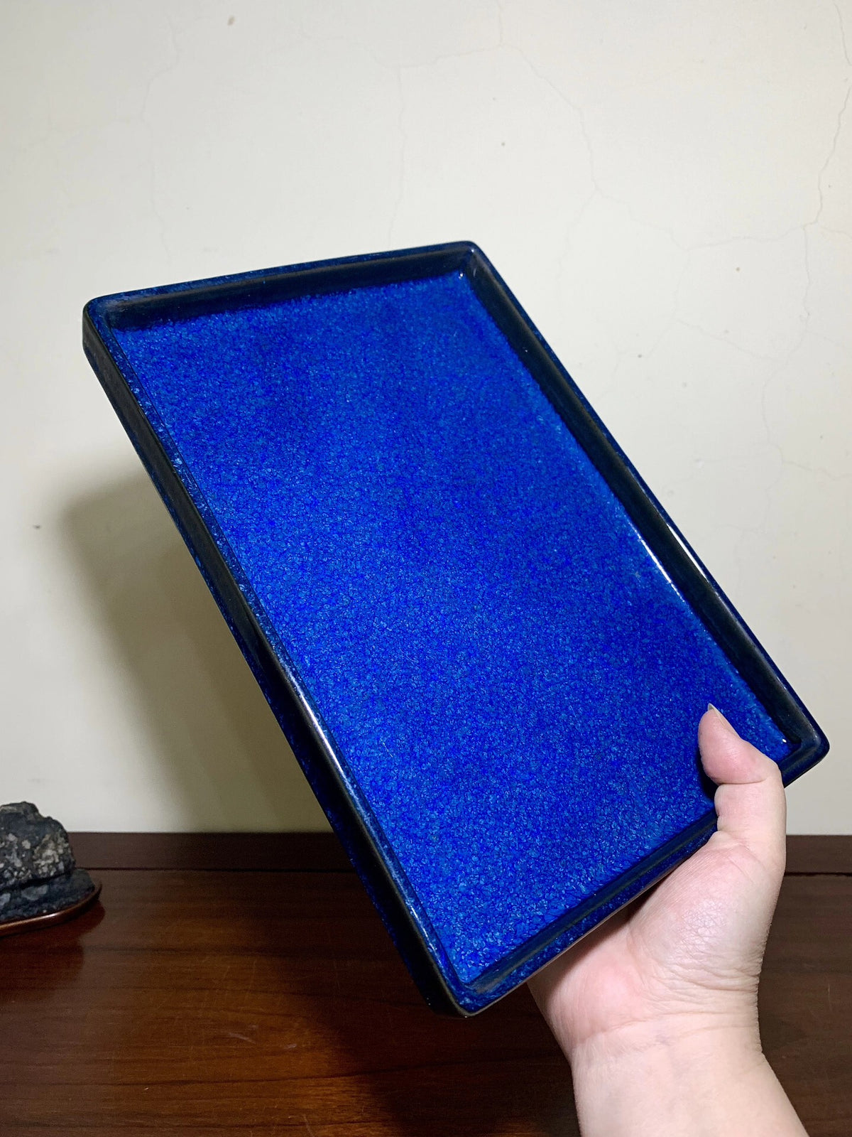 A hand holds a rectangular, glossy cobalt blue glazed tray with a slightly raised rim.